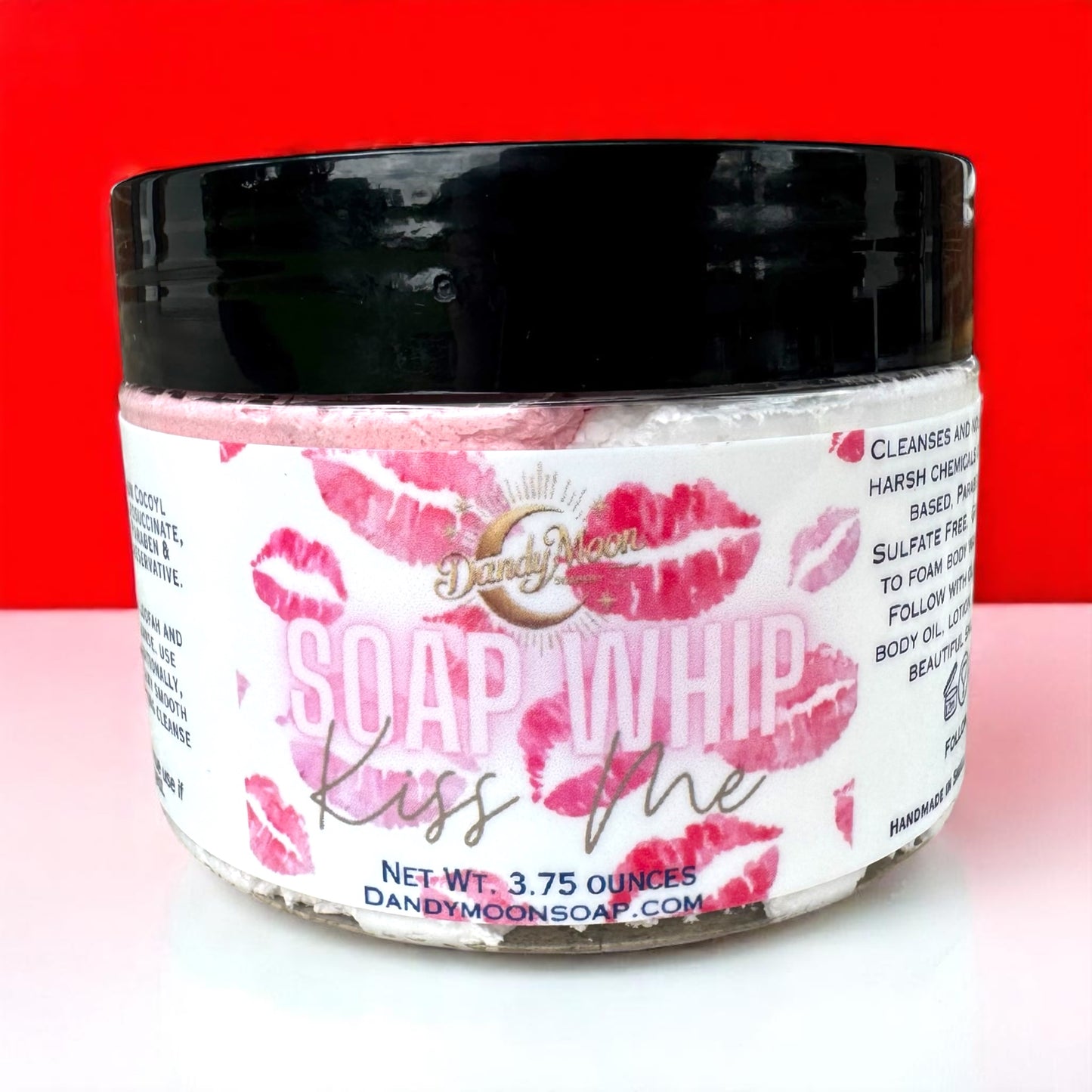 Jar of 'Soap Whip Kiss Me scent' product with pink lips label on a red background and a white surface