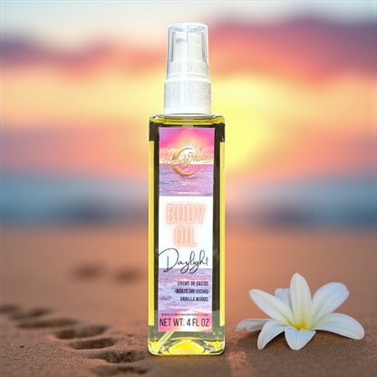 Body oil bottle with a colorful pink and purple label on a sandy beach with a white orchid sitting in the sand next to the bottle, with a blurred beach background