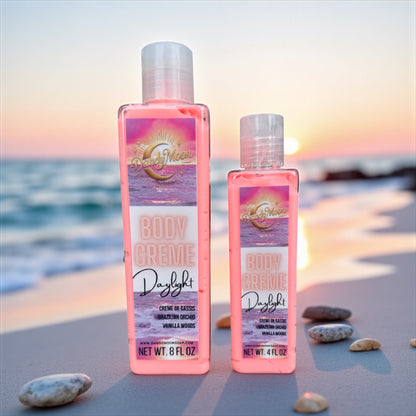 Two bottles of Daylight Body Crème Lotion, the lotion is a coral color in the clear bottle, standing on a sandy beach with a sunset in the background