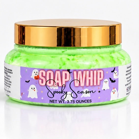 A jar of Halloween-themed 'Soap Whip'  in the scent 'Spooky Season' with bright green soap whip inside, a shiny gold lid, and a purple label decorated with ghosts and bats.