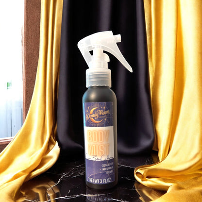 Bottle of Dandy Moon Body Mist on a black marble reflective surface with yellow and black silk curtains in the background