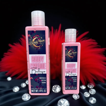 Two bottles of Dandy Moon Body Creme Lotion on a black satin background with red feathers and diamonds scattered around the bottles