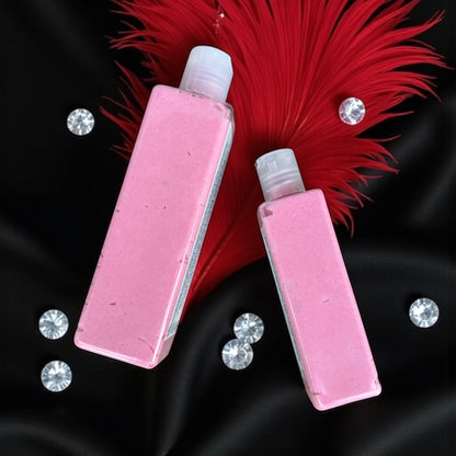 Two bottles of pink lotion laying on silk black fabric with red feathers and white diamonds scattered around them. 