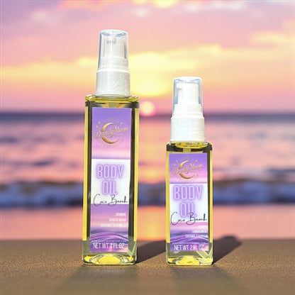 Two bottles of body oil, one is 2 ounces and one is 4 ounces, sitting on a sandy beach with a sunset on the ocean in the background
