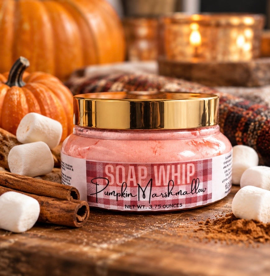 A jar of 'Soap Whip' Pumpkin Marshmallow soap whip styled on a rustic wooden surface with marshmallows, cinnamon sticks, and pumpkins in the background.