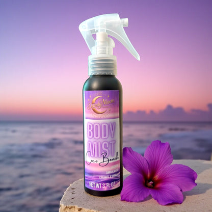 Body mist spray bottle with a purple flower next to the bottle, against a beach background