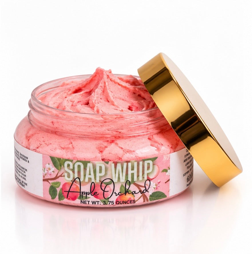 A jar of pink whipped body soap with its gold lid leaning against it on a white background. The label reads 'SOAP WHIP Apple Orchard' with Apple and floral graphics on the soap Whip label.
