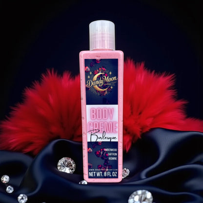 Bottle of Dandy Moon Body Creme lotion in Burlesque scent with red feathers and crystals on a satin and silk dark background