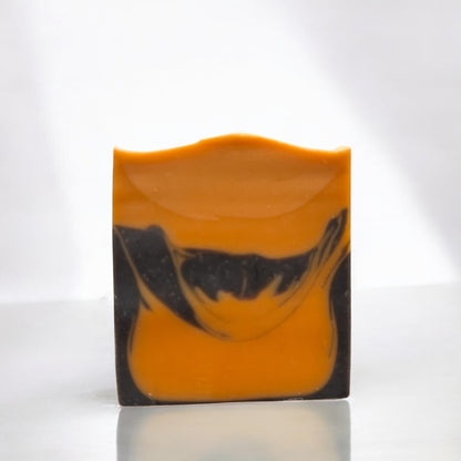 A bar of soap with a black and orange color design, sitting on a white surface against a white background
