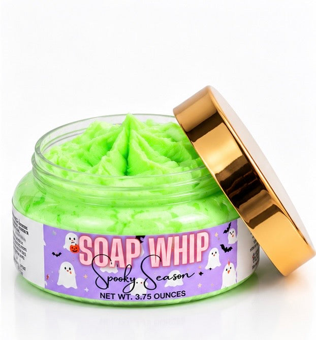 A jar of bright lime green whipped body soap with its metallic gold lid propped open, featuring a purple Halloween-themed label that reads 'SOAP WHIP Spooky Season'.