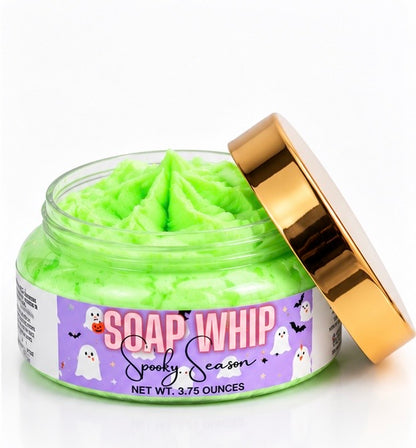 A jar of bright lime green whipped body soap with its metallic gold lid propped open, featuring a purple Halloween-themed label that reads 'SOAP WHIP Spooky Season'.
