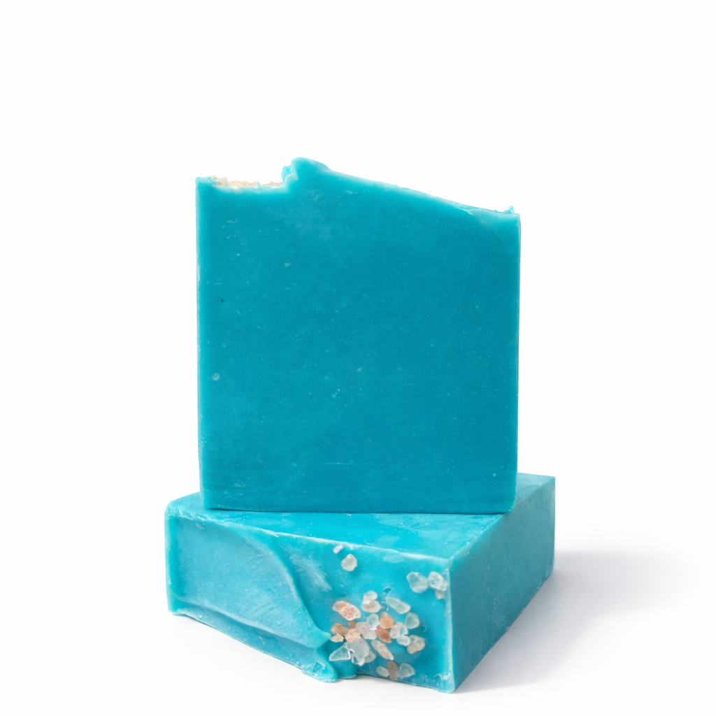 Two bars of blue soap, one is laying flat on its side to showcase the top design with himalayan sea salt top embeds, the other stands on top of that bar, with sea salt on a white surface against a white background.
