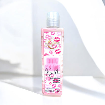 Bottle of 'Kiss Me' body creme lotion with pink and red lips on the lotion bottle label. the lotion bottle is clear with reddish pink and white lotion inside the bottle. it stands on a white surface against a white background