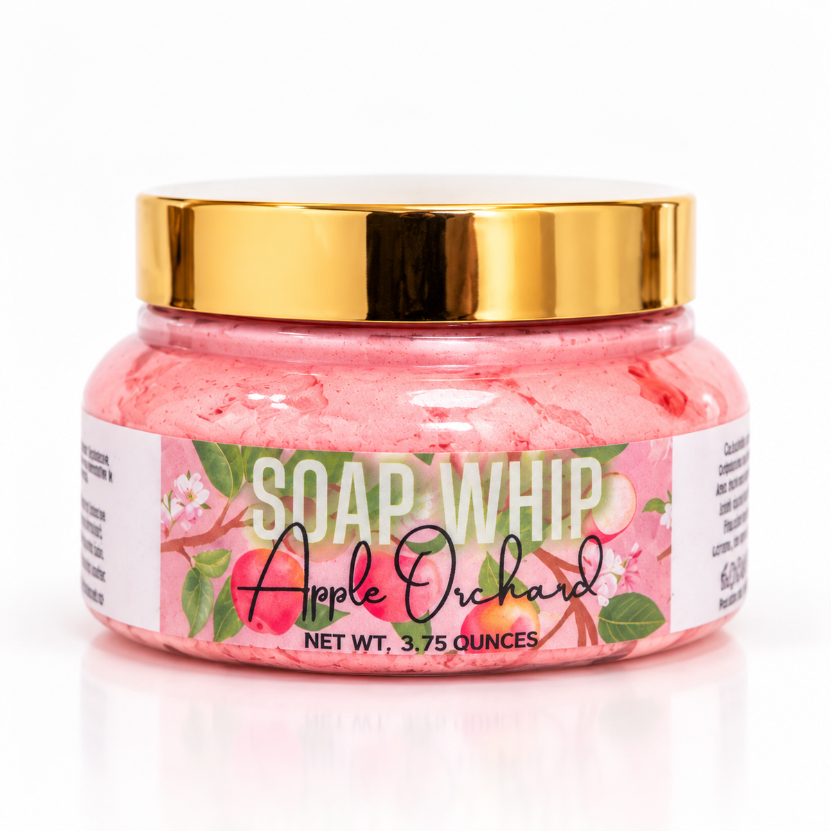 A jar of Soap Whip 'Apple Orchard'  with reddish whipped soap inside, a shiny gold lid, and a white label decorated with pink apples and green leaves, set against a clean white background.