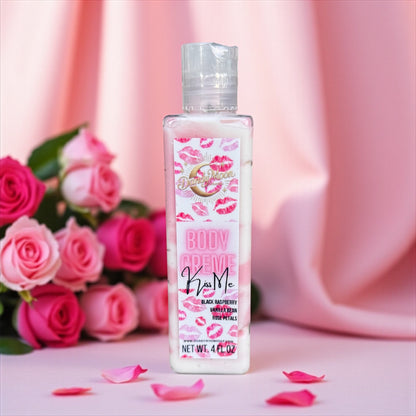 Bottle of 'Kiss Me' body creme lotion with pink roses and petals on a pink background
