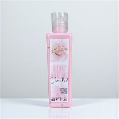a bottle of body creme lotion in the scent drenched stands on a white surface against a white background. the lotion inside the clear bottle is pink. 