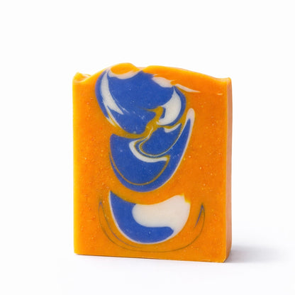 Bar of soap that is bright orange with blue and white swirl pattern on a white surface against a white background