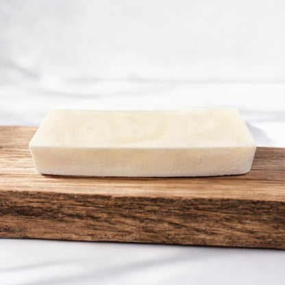 a single white stain stick, rectangular in shape, sits on a wooden surface, the wooden surface is sitting on a white surface as well, and all are against a white background.