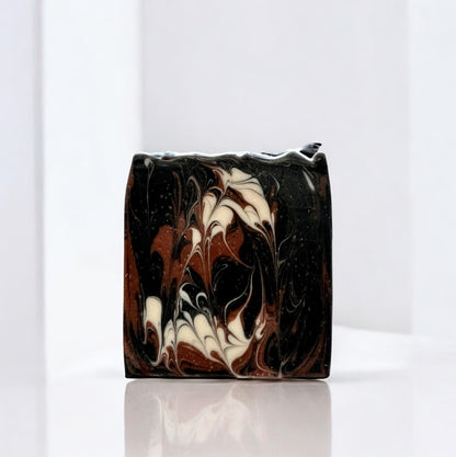 A bar of soap with swirls of black, brown, and white sitting on a white surface against a white background