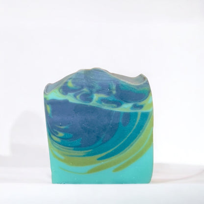 a bar or soap with cascades or light blue, green, and dark blue swirls. sitting on a white surface against a white background