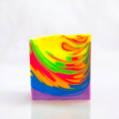 A multicolored bar of soap with a neon rainbow wave design, displayed against a white background on a white surface