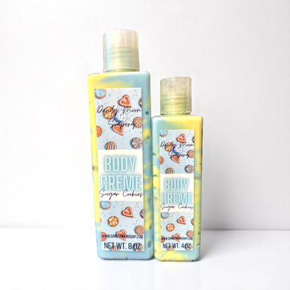 Two bottles of Body Creme Lotion in the scent Sugar Cookies stand on a white surface against a white background