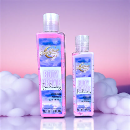 Two bottles of Dandy Moon body creme lotion in the scent enchanting. the bottles are clear and the lotion inside is swirls of pink and purple. they are on a light purple reflective surface with a pink and purple background and soft pink clouds behind the bottles.  