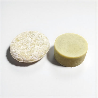 a round green shampoo bar and a round green conditioner bar sit on a white surface against and white background