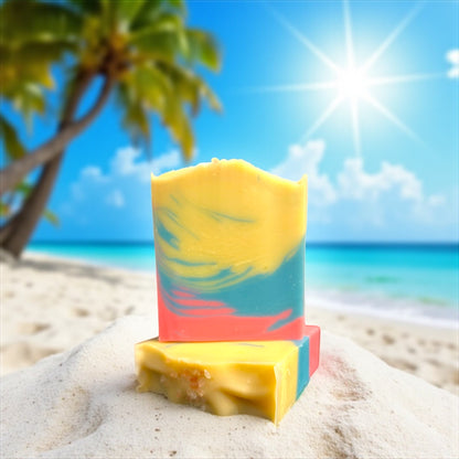 two Colorful yellow, blue and pink soap bars, one sitting on top of the other, on a sandy beach with palm trees and blue sky in the background