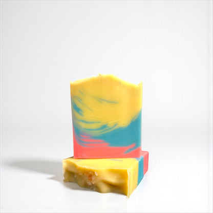 two Colorful soap bars, one sitting on top of the other, with a gradient from yellow to blue to pink on a white background