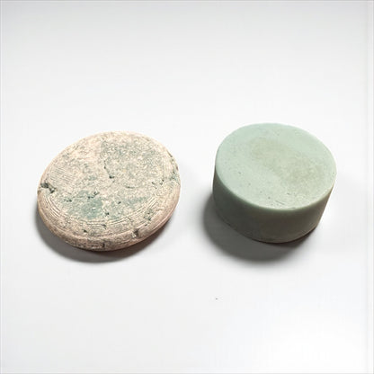 a light blue round shampoo bar and a light blue conditioner bar sit on a white surface in front of a white background 