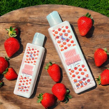Two bottles of Strawberries & Cream Body Creme Lotion laying on a flat surface and fresh strawberries scattered around the bottles. there is grass in the background. The bottles are clear and the lotion inside is swirls of red and white. 