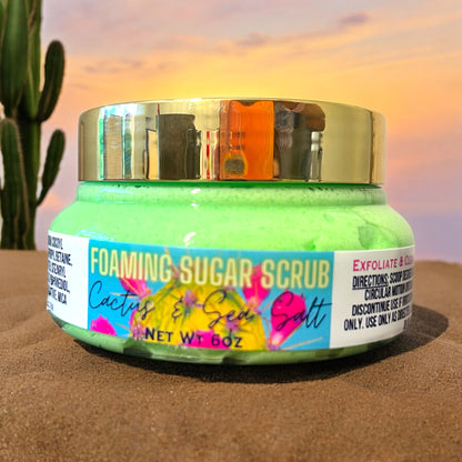 a jar of bright green foaming sugar scrub with a gold lid. sitting in desert sand with a cactus in the background and the sun setting over the horizon.