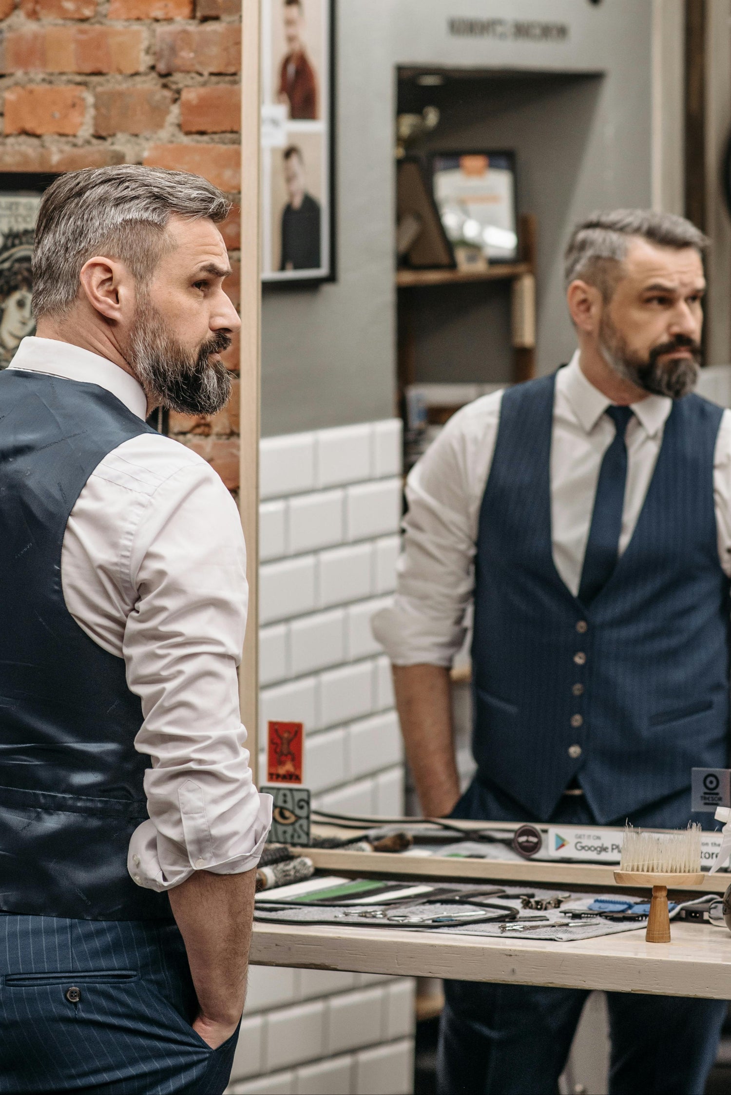 Man in a barbershop looking at himself in the mirror, wearing a blue vest and tie.